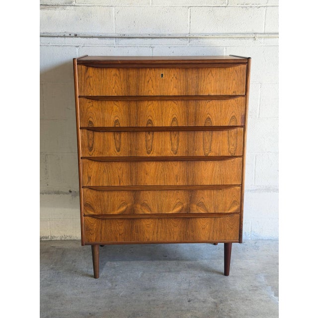 Six stacked drawers set above round tapered legs offer vertical storage. Sculpted lip handles span each drawer front for a...