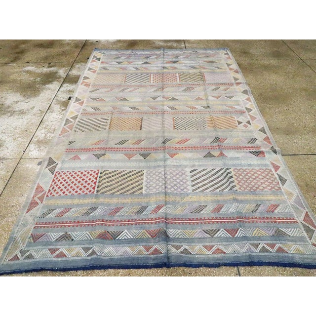 A vintage Moroccan Folk Kilim flatweave from the late 20th century. Slate blue, yellow, red, black, and white are among...