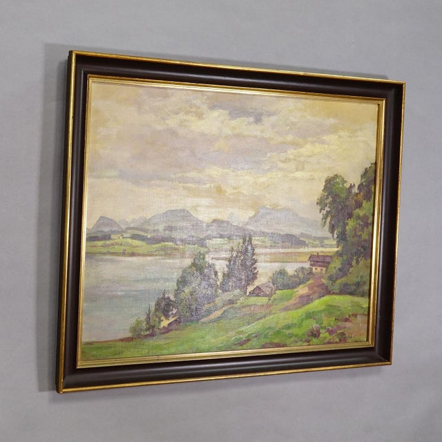 Alpine Lake View Oil Painting with Tyrolean Hut A large landscape painting in a dark brown frame with a gold inner lining....