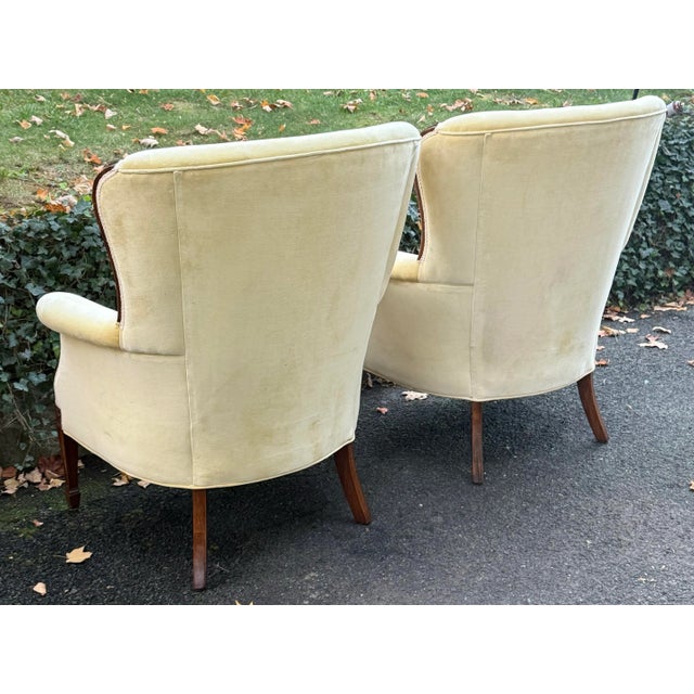 Stately pair of wingback chairs with tufted back, tapered legs with carved medallion detail, rolled arms and loose seat...