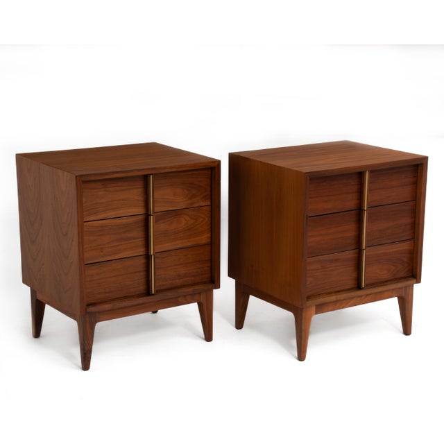 A pair of American of Martinsville three drawer nightstands, ca. 1960s. Walnut with a brass detail on the handles....