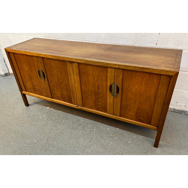 This vintage mid-century modern credenza by Henredon Furniture features a warm walnut finish and distinctive brass...