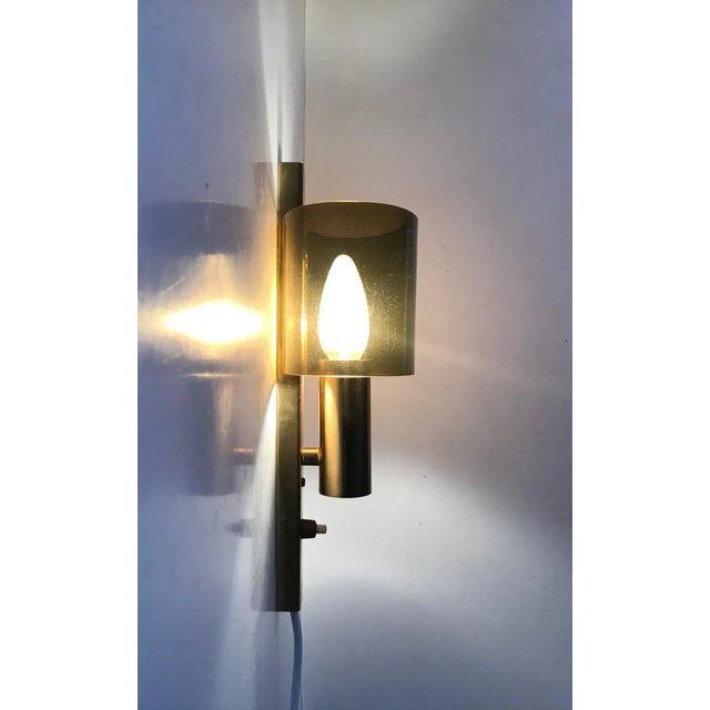 A stylish wall light composed of gilded brass holding an ovale shade in smoked acrylic glass. Designed and manufactured by...