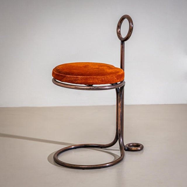 Sculptural stool made of tubular metal with a copper-toned alloy finish and a round seat cushion upholstered in burnt...