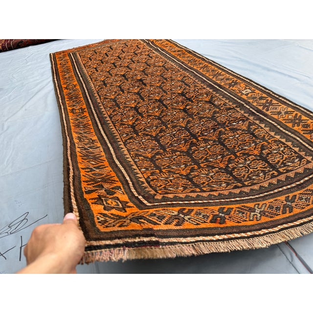 A vintage hand-knotted Baluch rug, worked on a dark aubergine-brown field in madder rust, camel and ivory. The Baluch are...