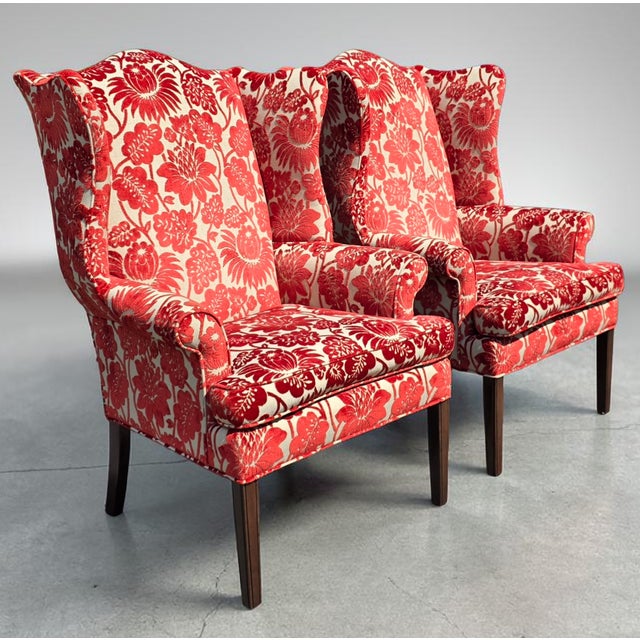 A striking pair of English-style wingback lounge chairs featuring dramatic red and ivory floral velvet upholstery. The...