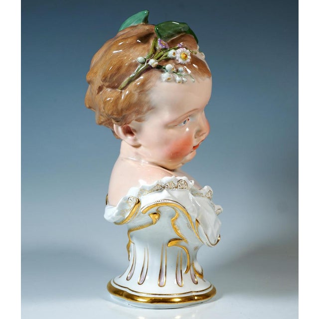 Very rare bust of a cherub wrapped in white cloth with gold trim, his blond curls adorned with delicate spring flowers and...