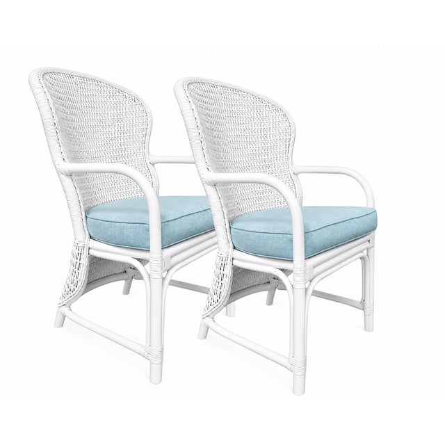 Charming pair of vintage white wicker rattan armchairs featuring a classic coastal silhouette with gently curved arms and...