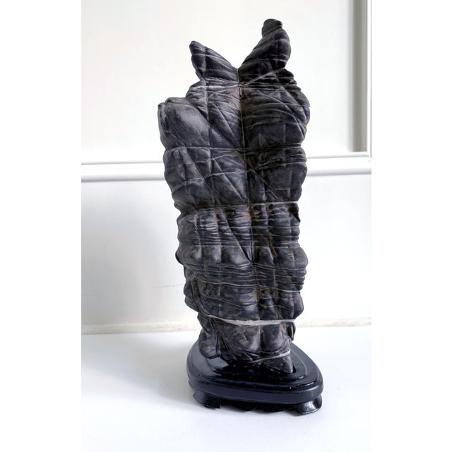 A Chinese scholar stone of Lingbi type presented on a carved wood base. This stone takes a singular vertical form with one...