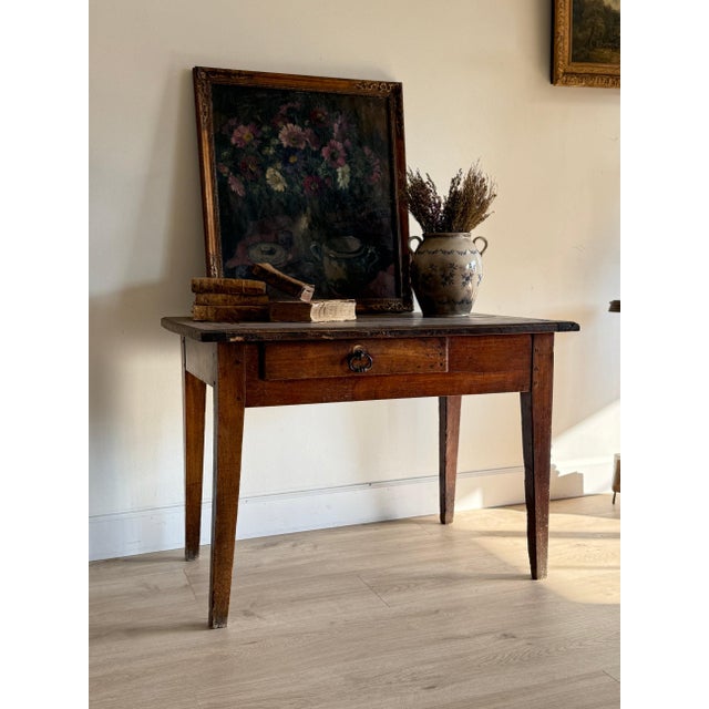 A French farmhouse table with a single drawer and original pull, tapered square legs, and a warm walnut-brown top showing...