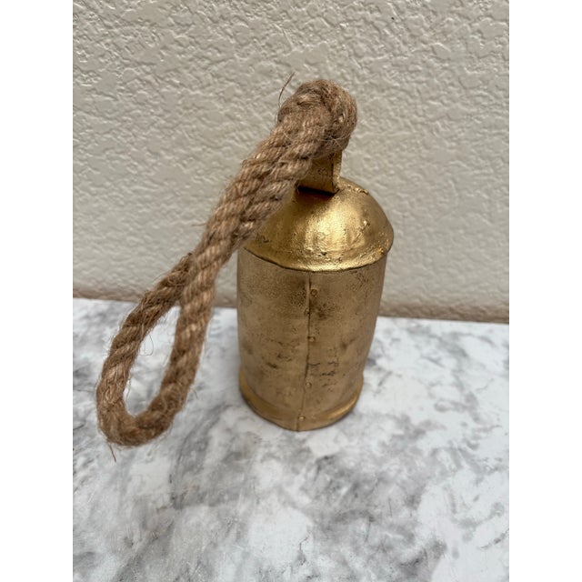 Rustic gold toned metal large cowbell with rope handle. Fun farmhouse or cabin accent for indoor and outdoor decor.