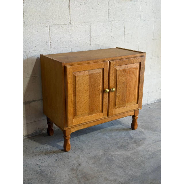 Two paneled cabinet doors open to reveal an interior storage shelf above turned legs. Brass fluted knobs add subtle detail...