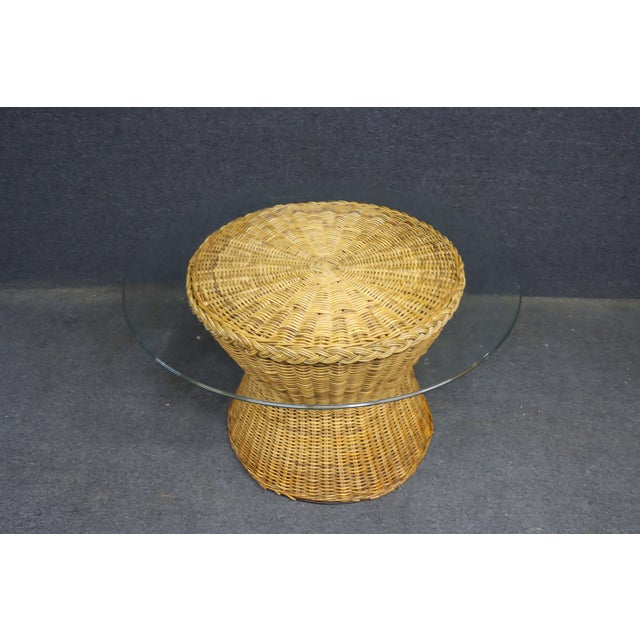 Mid-century modern wicker coffee table featuring a sculptural hourglass-shaped base in woven natural wicker. The rounded...