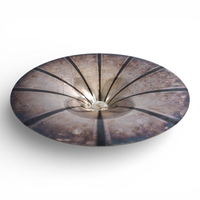 This silver-plated, sculptural brass bowl, with its conical shape and dark rays radiating from the center, exudes absolute...