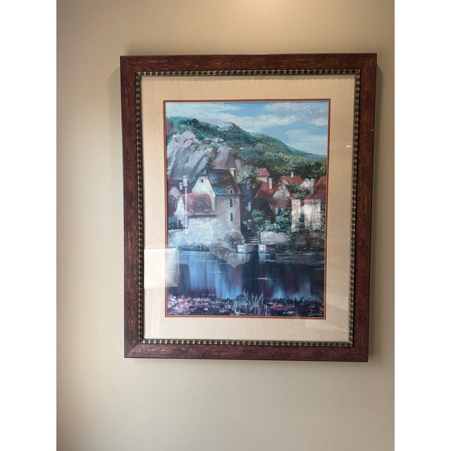 Framed print of a European village scene signed “Duval.” This vintage artwork depicts stone cottages with red roofs...