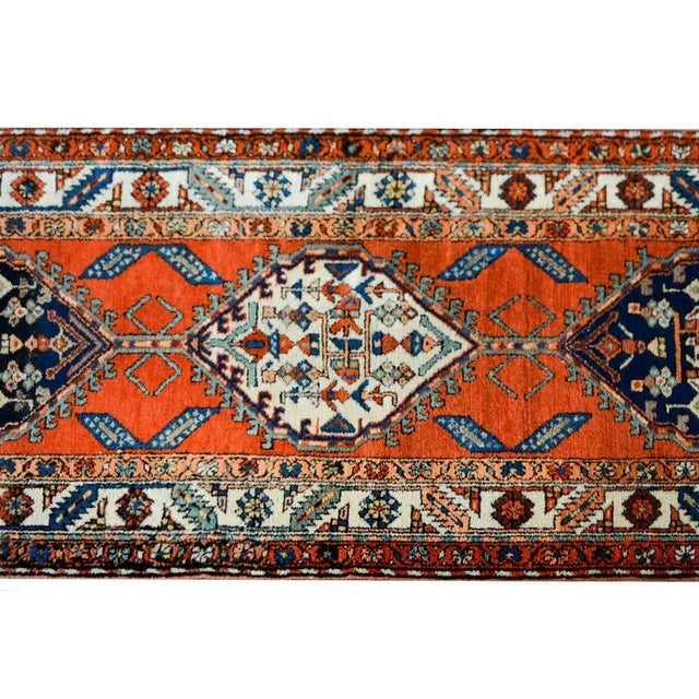 A bold early 20th century Persian Malayer runner with several diamond medallions against a crimson background and...