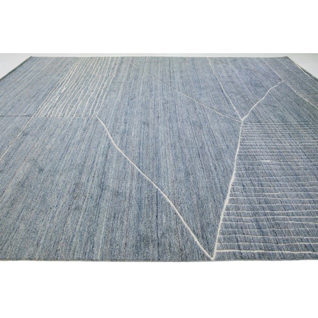 This luxurious wool rug features a timeless Moroccan pattern in a contemporary abstract Minimalist style, utilizing blue...