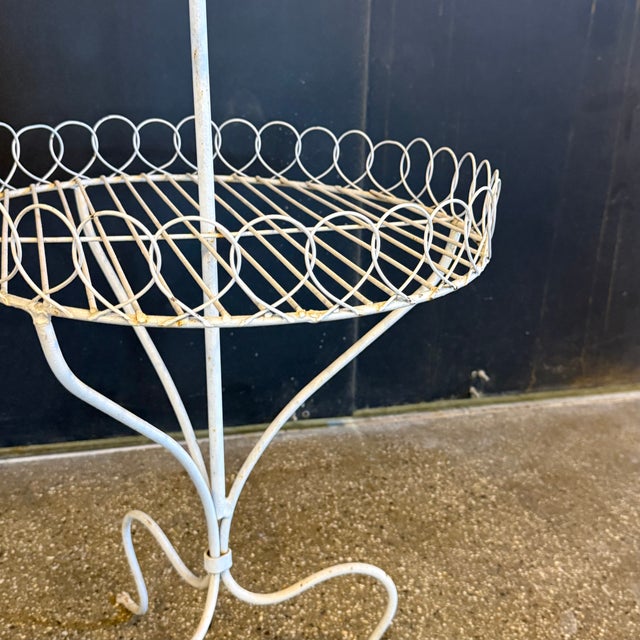 This charming vintage plant stand features a white-finished wrought iron frame with two tiered circular shelves bordered...