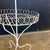 This charming vintage plant stand features a white-finished wrought iron frame with two tiered circular shelves bordered...