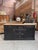 This antique sideboard has been fully restored. It features a black-patinated body and a raw wood top. It has two large...