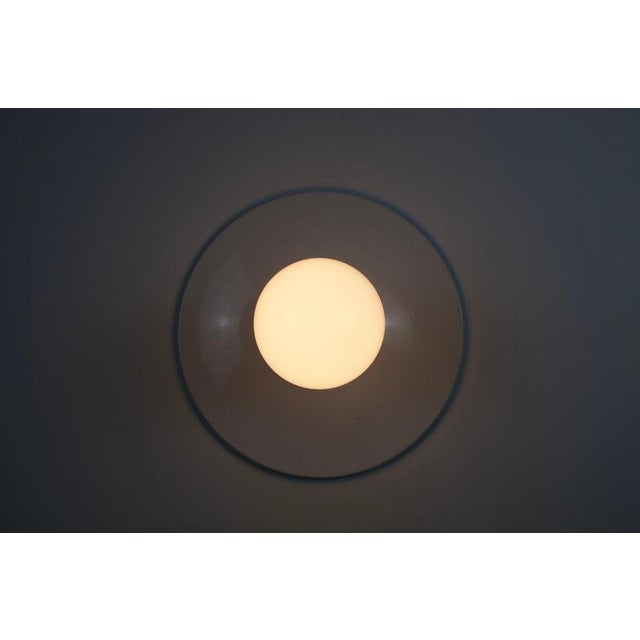 Italian wall lamp or flush mount from the 1960s with a clean white disc-shaped base and a central opaline glass globe. The...