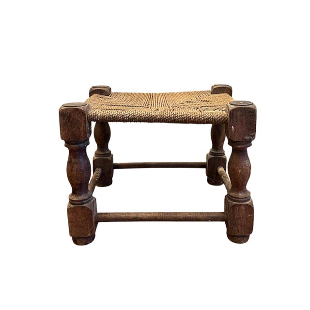 A charmingly quirky antique footstool. Features a solid wood frame with a woven, seagrass rope seat. Handmade in a folk...
