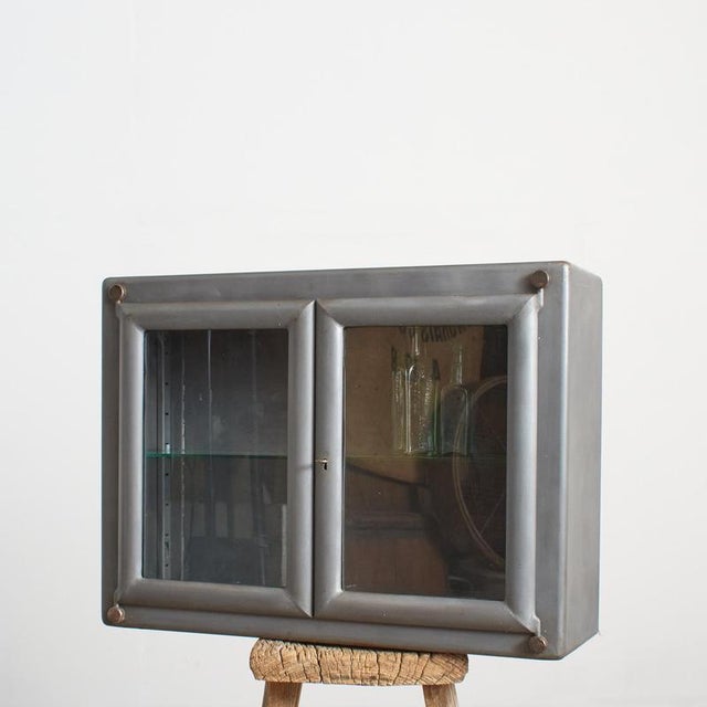 An antique metal medical wall cabinet from dental surgery in the Czech Republic, the cabinet has a pair of glazed doors...