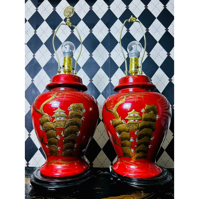 Pair of vintage chinoiserie table lamps featuring red lacquered ceramic bodies with raised landscape and pagoda motifs...