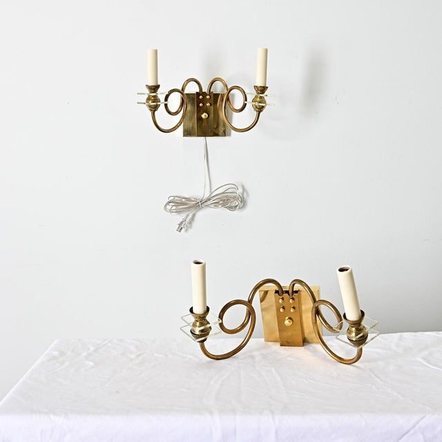 A pair of vintage mid-20th century French wall sconces in brass and glass with expressive loops that give them character...