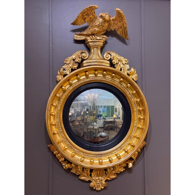 A large and impressive English Regency period carved giltwood convex mirror with a spread wing eagle perched on a stepped...
