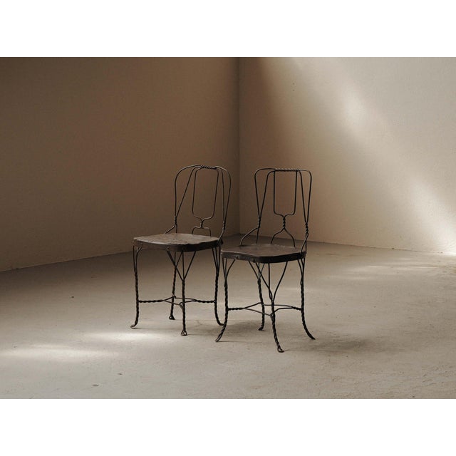 Pair of chairs with sculptural welded steel frames composed of curved and twisted rods. Their free-form lines give them a...