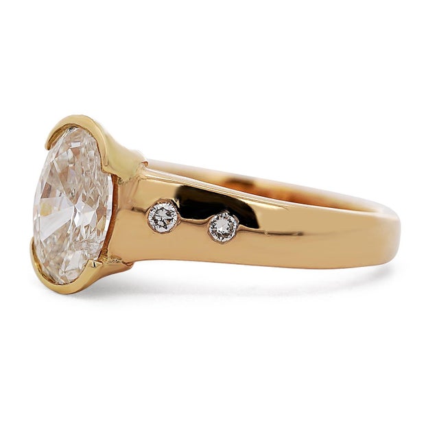 14K yellow gold ring features a half bezel-set 1.70 carat oval cut natural diamond, J color and I1 clarity, flanked by...