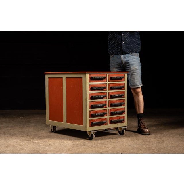 Vintage rolling wooden parts cabinet. This piece features 12 drawers of uniform size, and a gray frame with red drawers...
