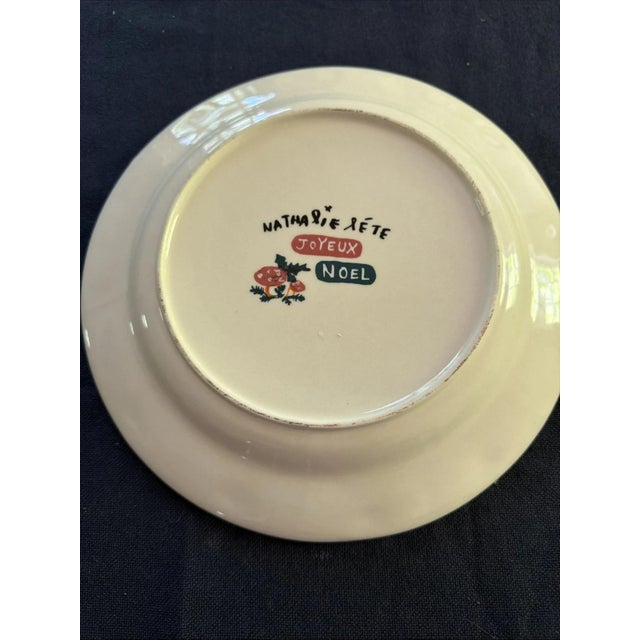 The Nathalie Lete Joyeaux Noël Dinner Plate is a round ceramic plate featuring a polka dot pattern and a charming sheep...
