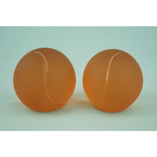 A delightful pair of tennis ball-shaped paperweights made of orange sandblasted glass, with added selenium and colloidal...