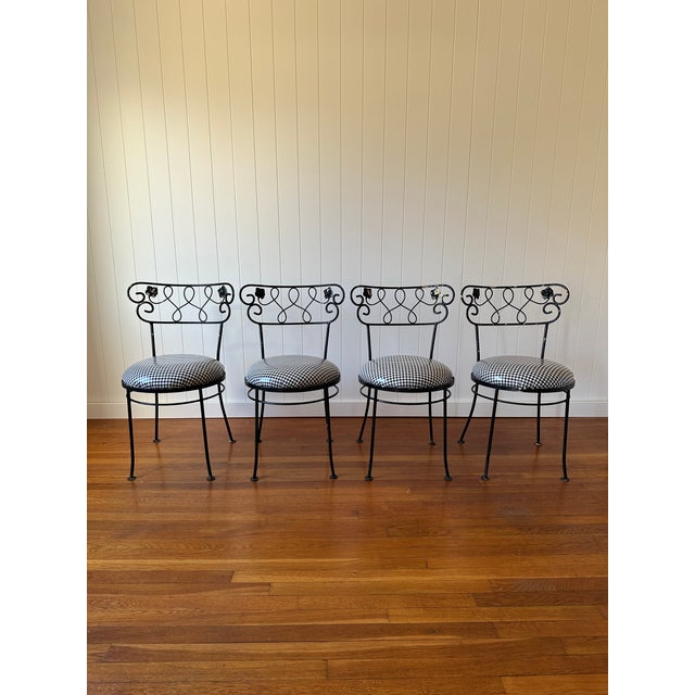 A set of four mid century wrought iron dining chairs with scrollwork backs and vinyl black-and-white gingham seats. Solid...