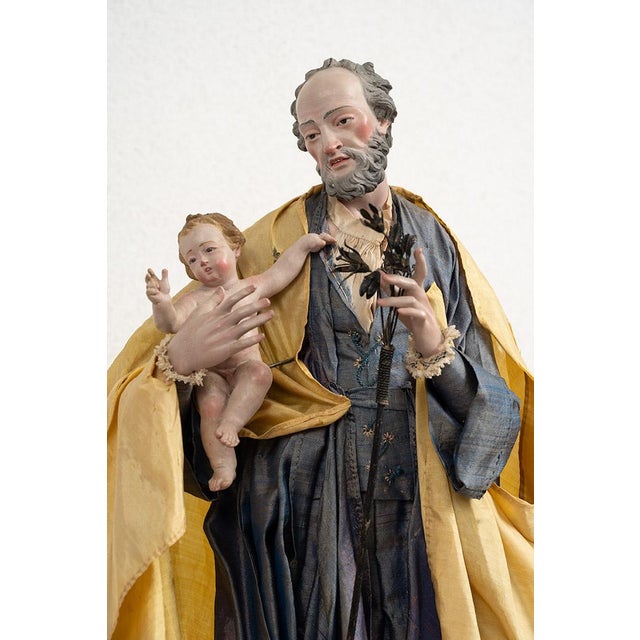Antique sculpture depicting Saint Joseph with Child resting on a gilded wooden base of the same period. The sculpture...