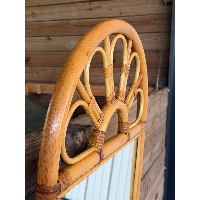 Charming vintage coastal rattan wall mirror featuring an elegant fan-back arch and integrated woven rattan display shelf....