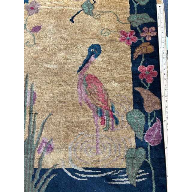A beautiful early 20th century Chinese art deco rug, with a camel ground and indigo floral border, featuring a wading...