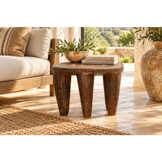 A low, oval seat of dark carved wood carries a field of incised triangles and crossed lines across its top, resting on...