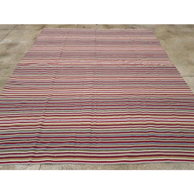 This Mid-20th century Turkish flatweave kilim rug, showcases a vibrant horizontal stripe pattern woven with a lively mix...