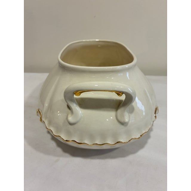 A charming vintage ceramic soup tureen featuring a soft cream glaze and elegant gold trim detailing. This classic serving...