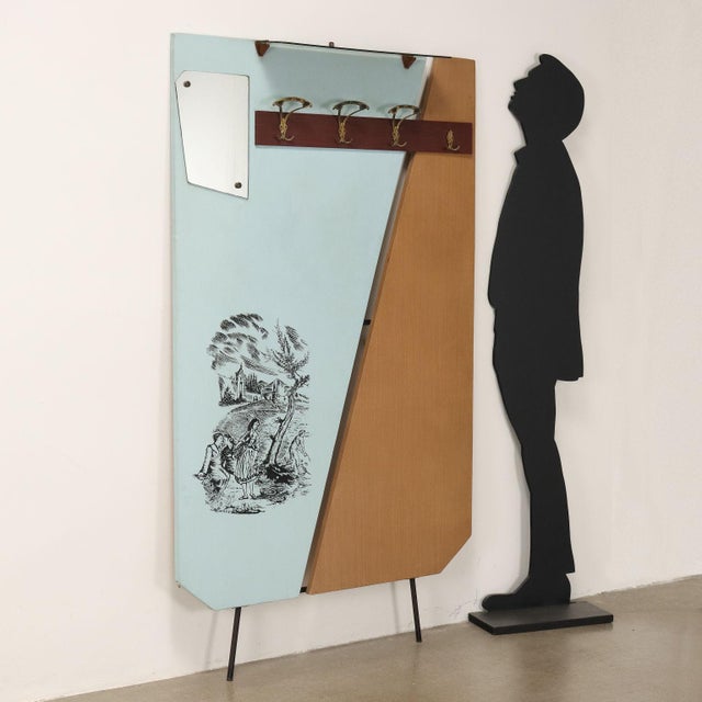 Wall-mounted coat rack with a wooden frame covered in vinyl, metal, brass, and mirror. One hanger is missing. This piece...