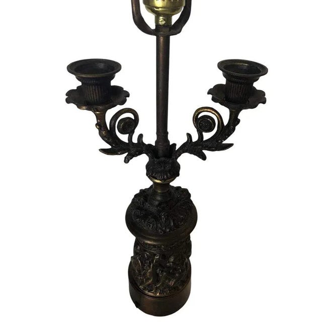 Neo-Classic Bronze Cherub Candelabra Table Lamp featuring a single light socket and Two Candleholders. The table lamp...