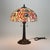 This table lamp exemplifies the Arts & Crafts movement, featuring a leaded stained glass shade and an ornate metal base....