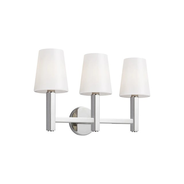 The Logan three light vanity fixture features tapered Milk White glass shades atop slim arms set along a horizontal beam...