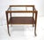 A teakwood framed rolling bar cart with glass inserted top , one end open to be used as a handle and a lower teak storage...
