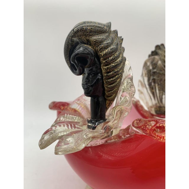 An artistic blown glass bowl with a rounded body in a shaded ruby ​​red, supported by a circular base in clear glass. The...