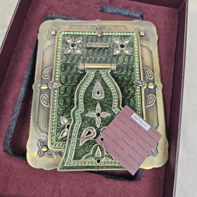 Presented in its original Michael Hero box, this ornate jeweled picture frame features green enamel-style detailing, gold-...