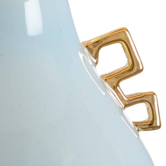 Metallic gold handles accent a large pear shaped powder blue glazed ceramic vase with square gold leaf base. Capped off...